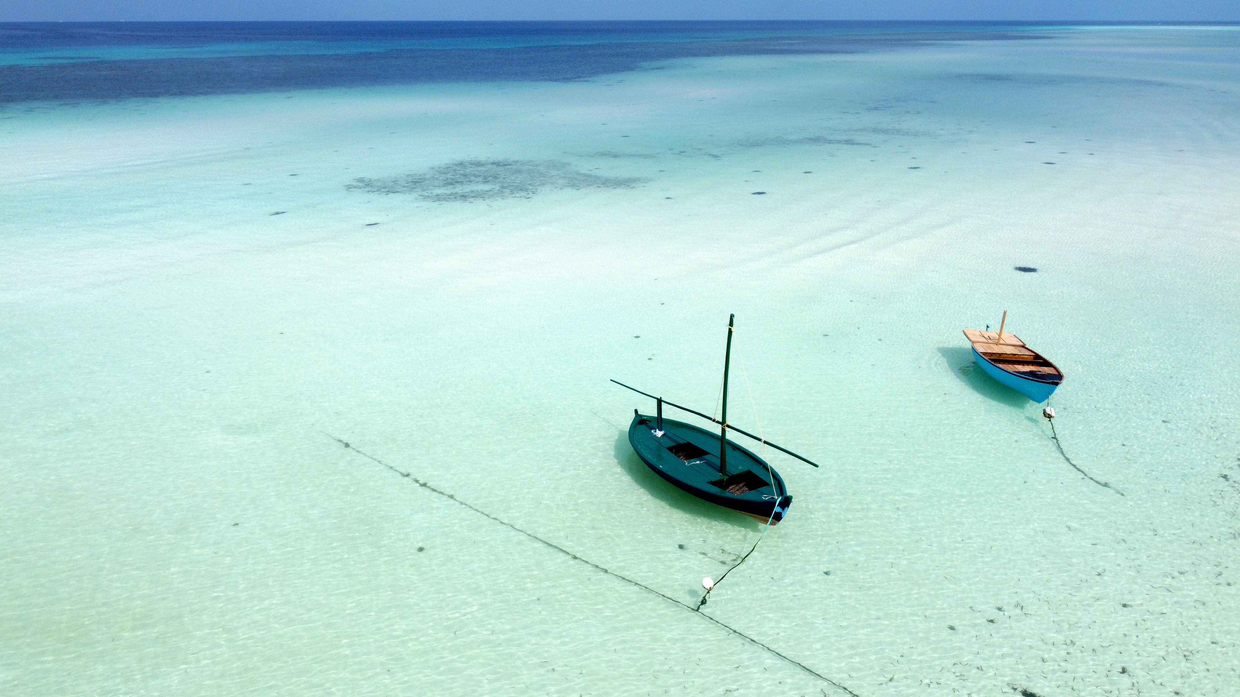 aerial view of Maldives ocean with the different shades of the ocean from tourqoise to aqua waters, with two small boats anchored near each other