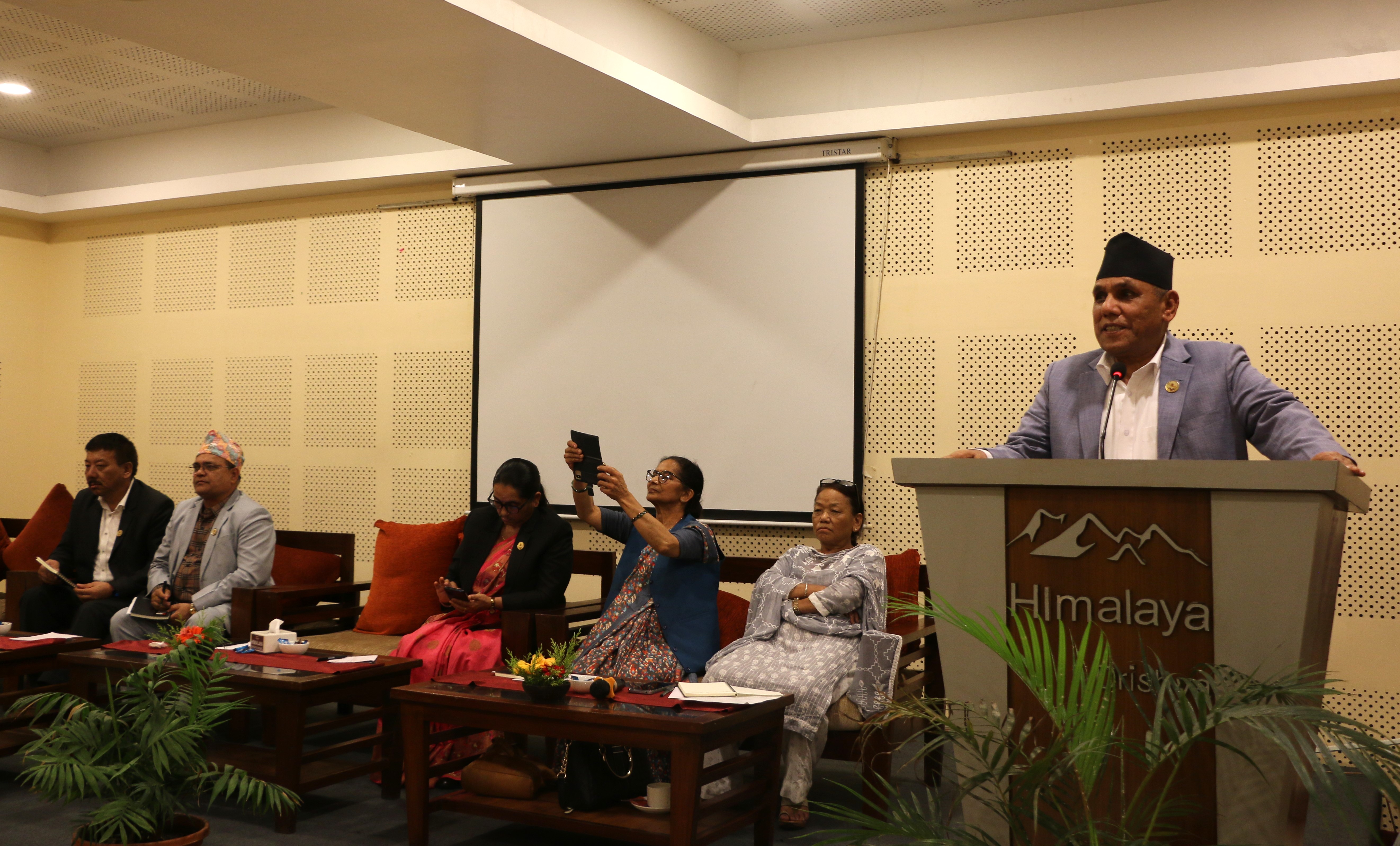 a man speaking at a podium in front of a panel 